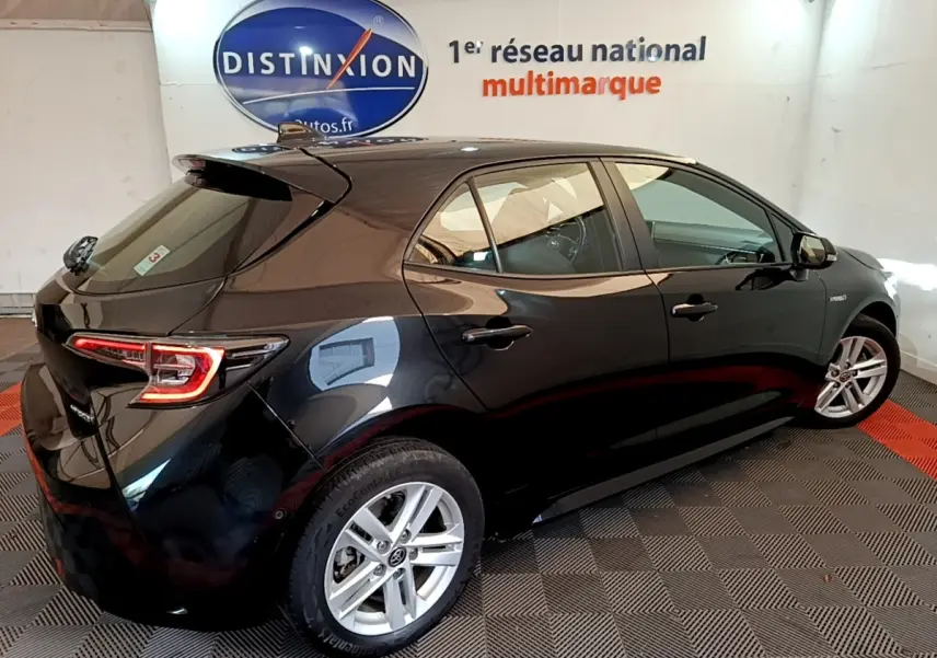 Toyota Corolla hybride noire vue 3/4 arrière droit en intérieur avec feux arrière LED et jantes alliage.
