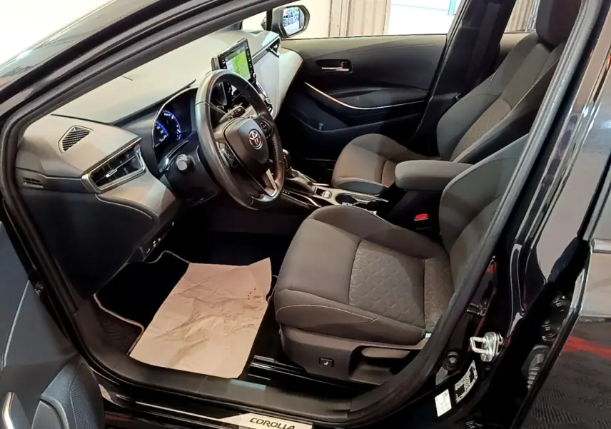 Intérieur noir de la Toyota Corolla hybride 2021 vu côté conducteur, avec tableau de bord et écran tactile visible.