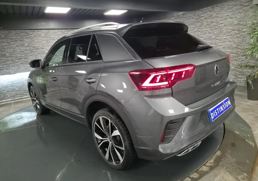 Vue 3/4 arrière droite d'un Volkswagen T-Roc gris métallisé avec feux LED allumés et jantes alliage noir et argent.