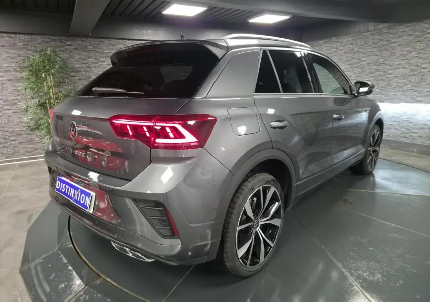 Volkswagen T-Roc 1.5 TSI Evo gris, vue 3/4 arrière droit, avec jantes alliage 19 pouces et feux LED allumés.