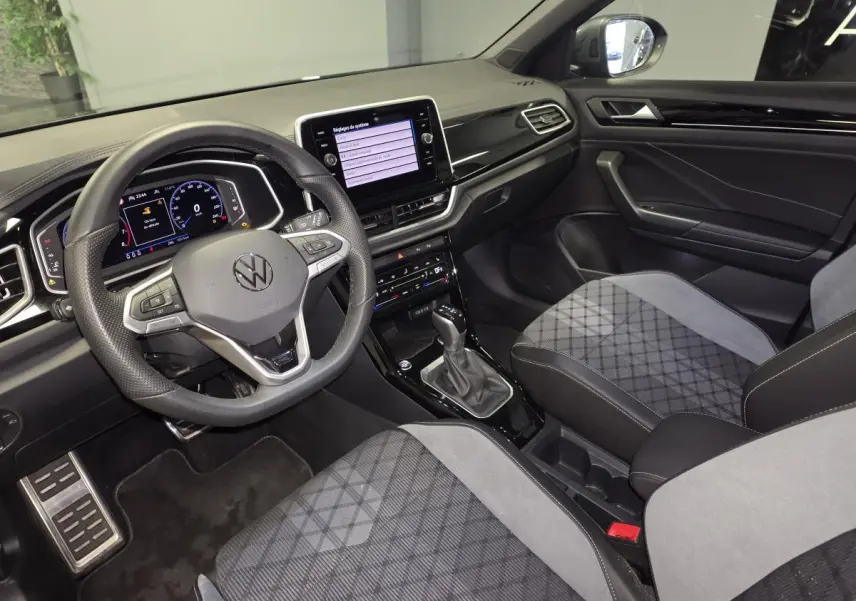 Intérieur avant du Volkswagen T-Roc 2025, vue côté conducteur, sièges gris et tableau de bord noir brillant.
