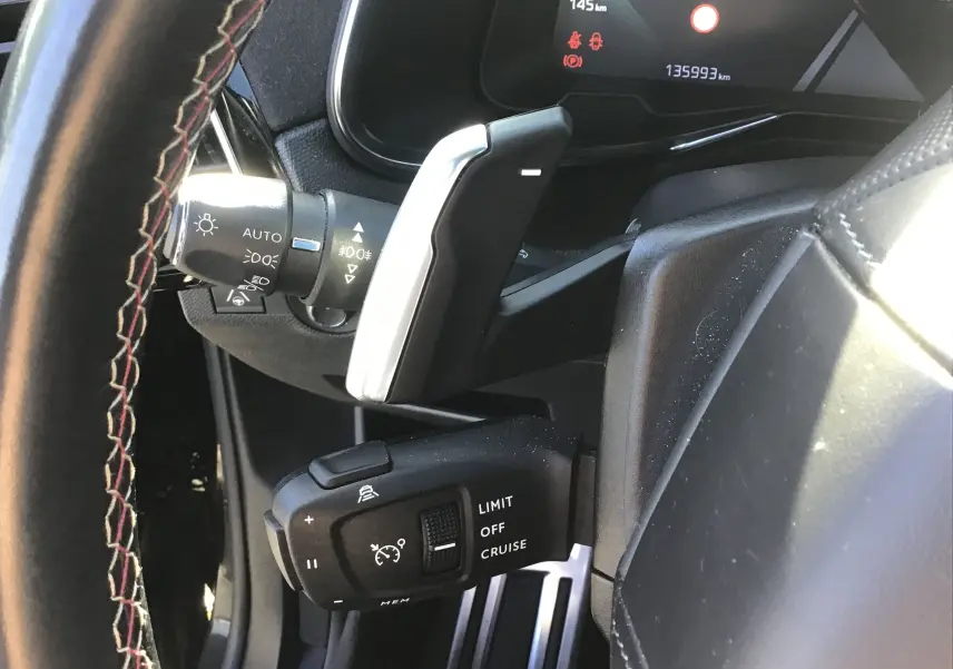 Gros plan sur la commande de régulateur de vitesse et le volant en cuir noir avec surpiqûres rouges du DS7 Crossback noir.
