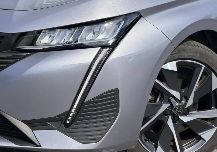 Gros plan sur l'avant droit gris Artense du Peugeot 308 SW 2025, mettant en valeur le phare LED et la jante alliage 17'' Halong.