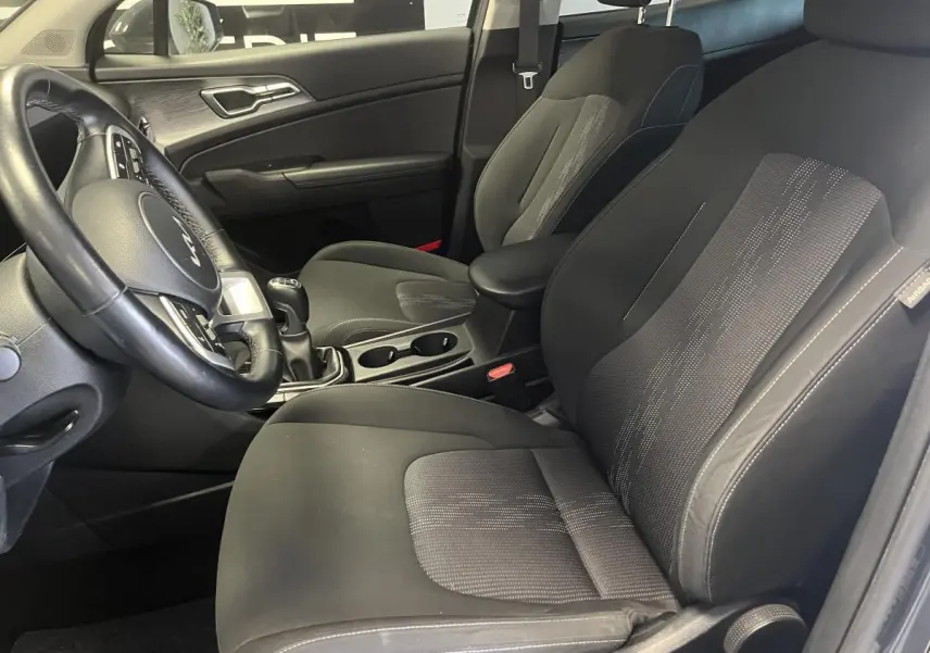 Intérieur avant du Kia Sportage 2022, sièges tissu noir, volant cuir et console centrale avec boîte manuelle.