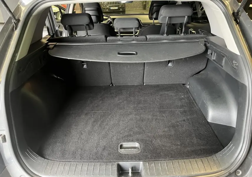 Coffre ouvert du Kia Sportage gris 2022, montrant le plancher plat et la plage arrière rétractable noire.