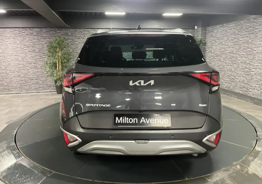 Vue arrière d'un KIA Sportage gris métallisé 2022 avec feux arrière LED et bouclier noir laqué en intérieur showroom.