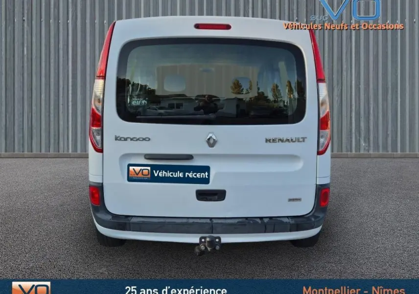 Vue arrière d’un Renault Kangoo blanc 2016 avec attelage et vitres surteintées, garé devant un mur métallique.