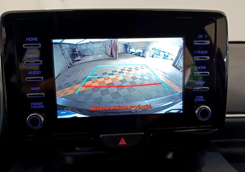 Écran tactile central affichant la caméra de recul de la Toyota Yaris hybride gris clair, avec lignes de guidage colorées.