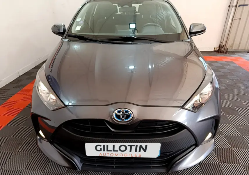 Vue frontale d'une Toyota Yaris hybride gris clair avec calandre noire et feux allumés en intérieur.