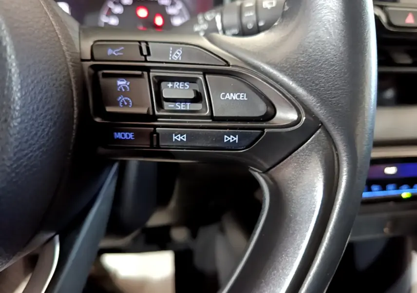 Gros plan sur les commandes du volant côté droit d'une Toyota Yaris hybride 2021, avec affichage numérique en arrière-plan.