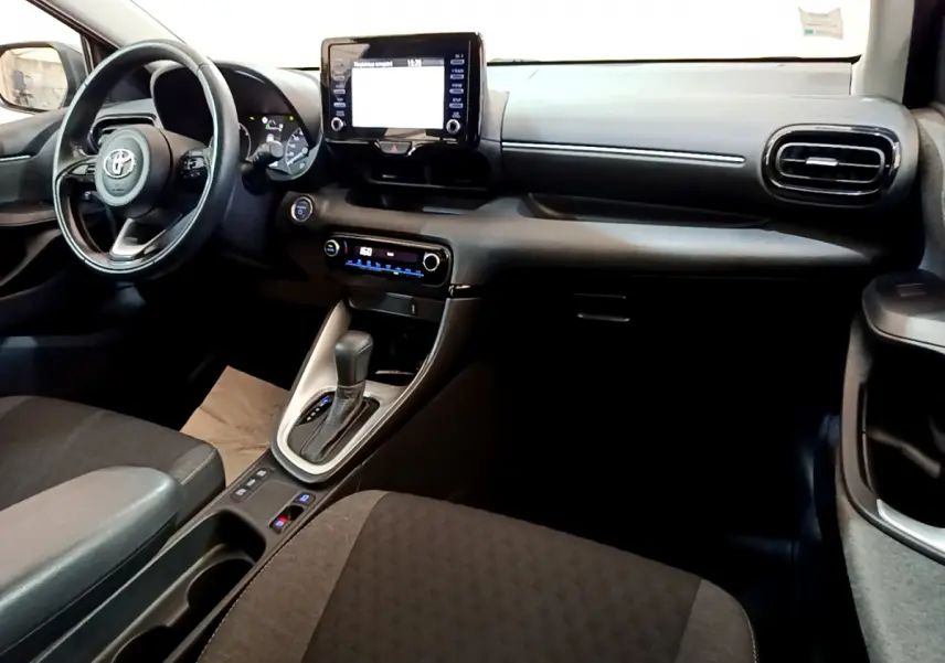 Intérieur avant droit de la Toyota Yaris Hybride 116h 2021, tableau de bord noir avec écran tactile central et volant cuir.