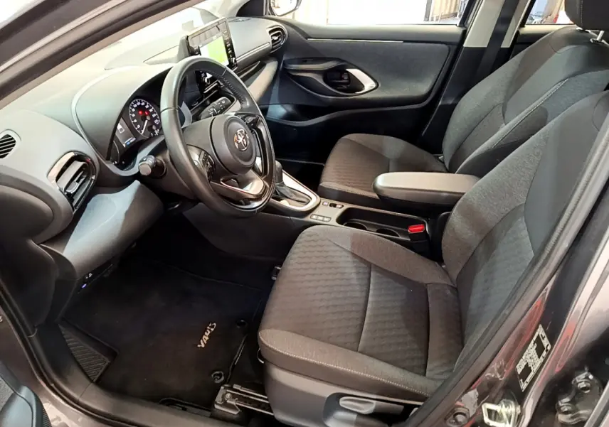 Intérieur avant droit d'une Toyota Yaris hybride 2021, sièges gris, volant cuir multifonctions et écran tactile central.