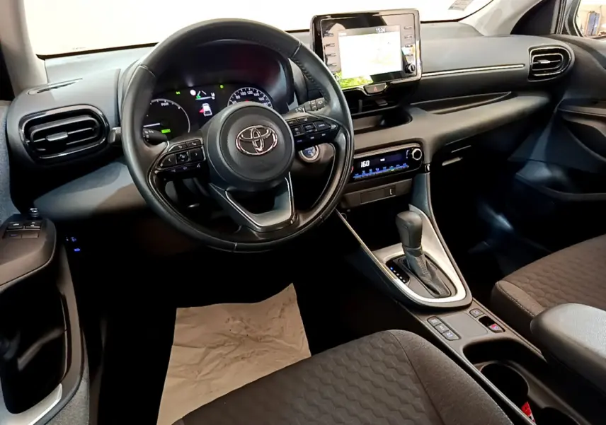 Vue intérieure de la Toyota Yaris hybride 2021, tableau de bord et volant cuir noir avec écran tactile central.