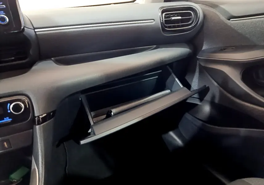 Intérieur de la Toyota Yaris Hybride 2021, vue côté passager sur la boîte à gants ouverte et tableau de bord noir.