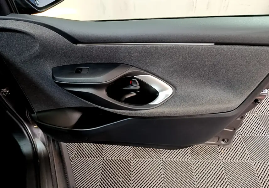 Porte intérieure côté gauche gris clair de la Toyota Yaris Hybride 116h avec poignée argentée et habillage tissu noir.