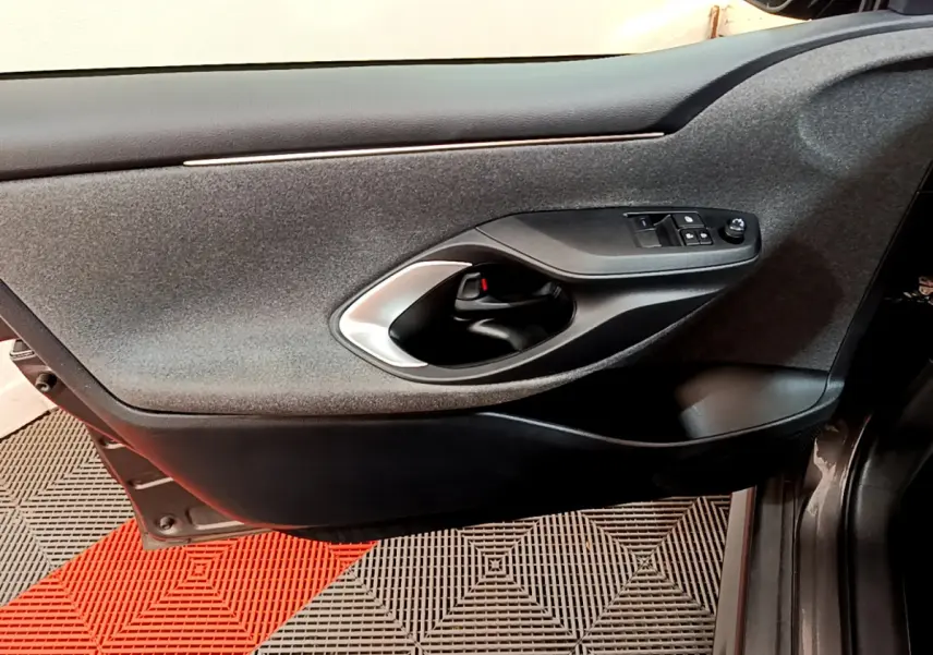 Gros plan sur la porte côté conducteur gris clair de la Toyota Yaris hybride 2021 avec commandes de vitres et poignée intérieure noire.