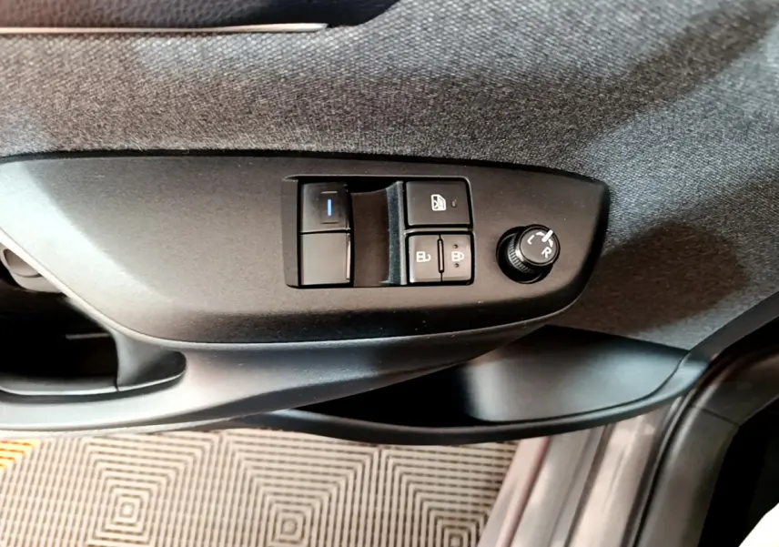 Gros plan sur les commandes de réglage des rétroviseurs et vitres côté conducteur de la Toyota Yaris hybride gris clair 2021.