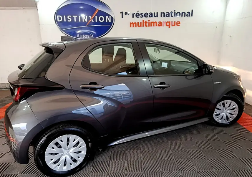 Profil droit d'une Toyota Yaris hybride gris clair 2021, avec jantes argentées et badge Hybride visible sur l'aile avant.