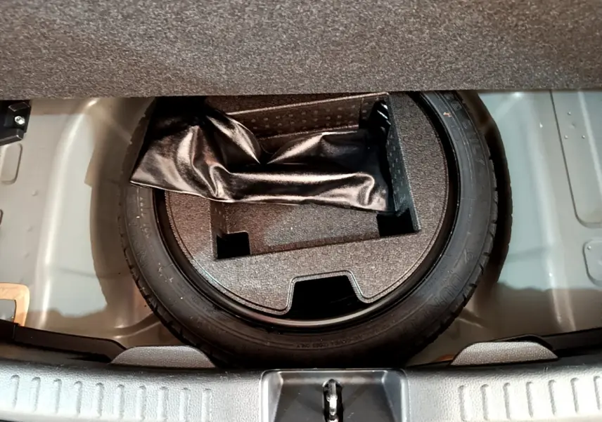 Pneu de secours et rangement sous le plancher du coffre d'une Toyota Yaris hybride gris clair, vue plongeante.