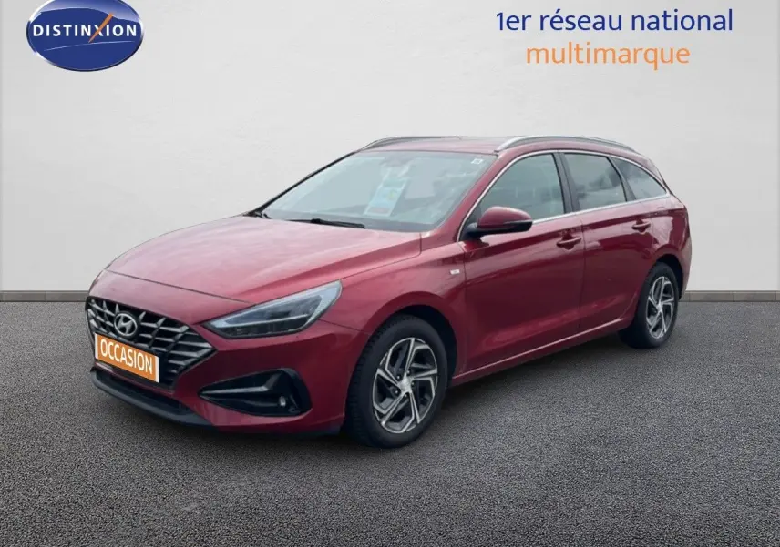 Vue 3/4 avant droite d'une Hyundai i30 SW 2023 Sunset Red Metal avec jantes alliage et calandre distinctive.