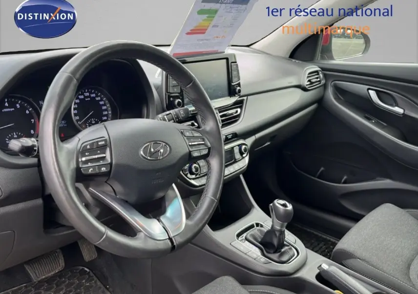 Vue intérieure côté conducteur de la Hyundai i30 SW 2023 avec tableau de bord noir et volant cuir multifonction.