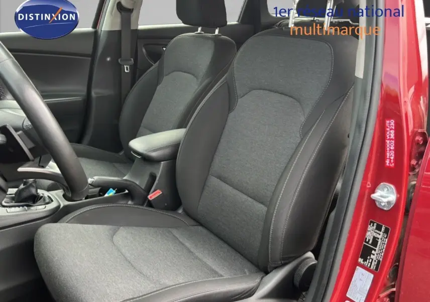 Vue intérieure côté conducteur de la Hyundai i30 SW rouge, mettant en valeur les sièges tissu gris avec surpiqûres noires.