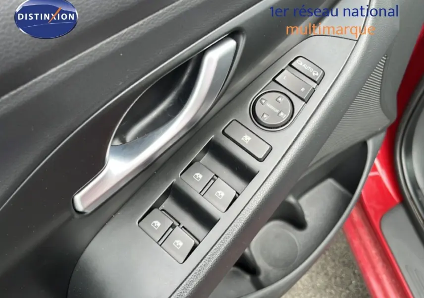 Gros plan sur la commande des vitres et rétroviseurs côté conducteur d'une Hyundai i30 SW rouge Sunset Red 2023.