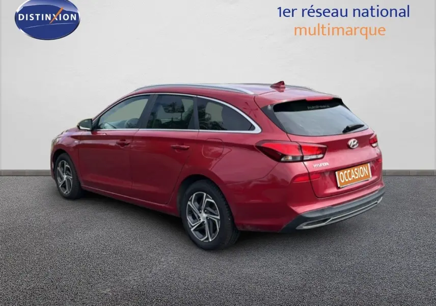 Vue 3/4 arrière droite d'une Hyundai i30 SW 2023 en rouge Sunset Red Metal avec jantes alliage bicolores.