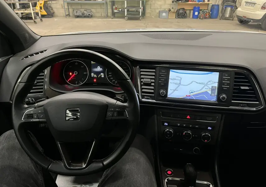 Vue intérieure centrée sur le volant et tableau de bord noir du SEAT Ateca blanc avec écran tactile et navigation affichée.