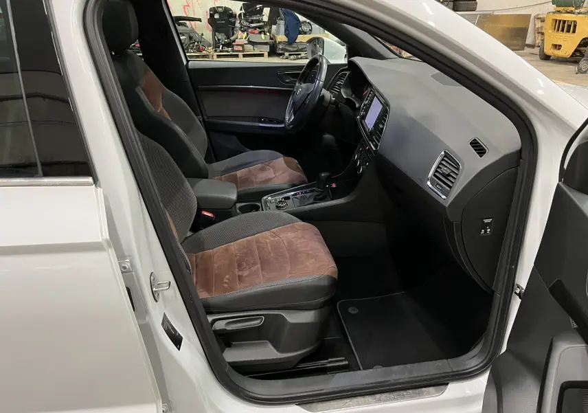 Vue intérieure côté conducteur du SEAT Ateca blanc 2016, sièges bi-matière marron et noir, tableau de bord moderne.