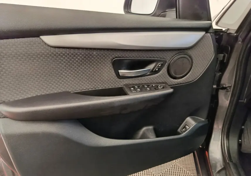 Vue intérieure côté gauche de la porte avant grise d'une BMW Série 2 Gran Tourer avec garniture tissu et commandes électriques.