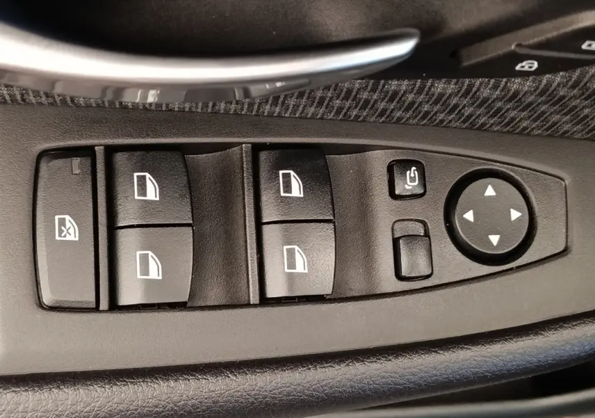 Gros plan sur les commandes de lève-vitres et rétroviseurs noirs dans la porte côté conducteur d'une BMW Série 2 Gran Tourer gris clair.
