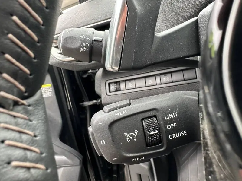 Gros plan sur la commande de régulateur de vitesse du Peugeot 3008 Hybride Rechargeable noir Perla Nera, côté gauche du volant.