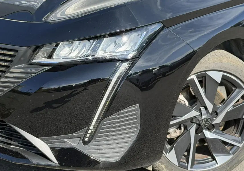 Gros plan sur l’avant droit noir Perla d’une Peugeot 308 SW 2025, mettant en valeur les phares LED et jantes alliage 17 pouces.