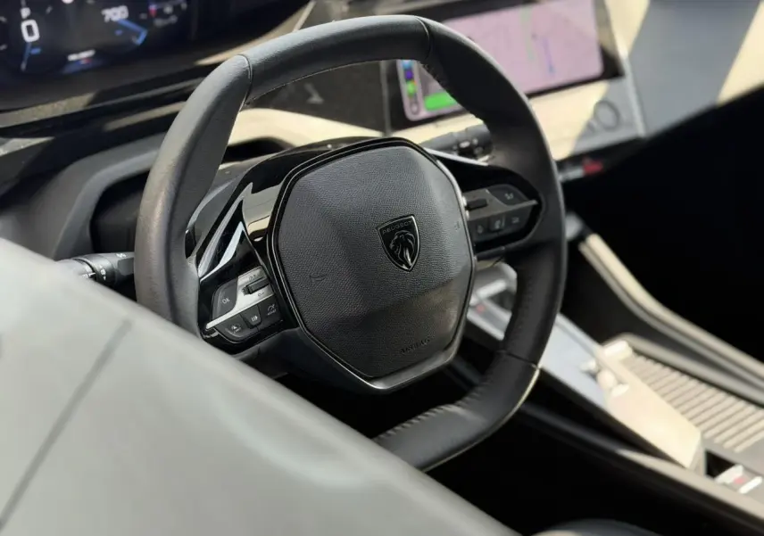 Vue rapprochée du volant cuir noir de la Peugeot 308 SW 2025 avec tableau de bord numérique et écran tactile central.