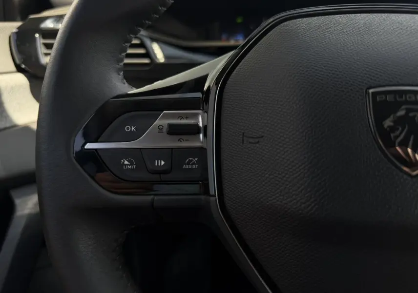 Gros plan sur la partie gauche du volant noir de la Peugeot 308 SW 2025 avec commandes du régulateur adaptatif.
