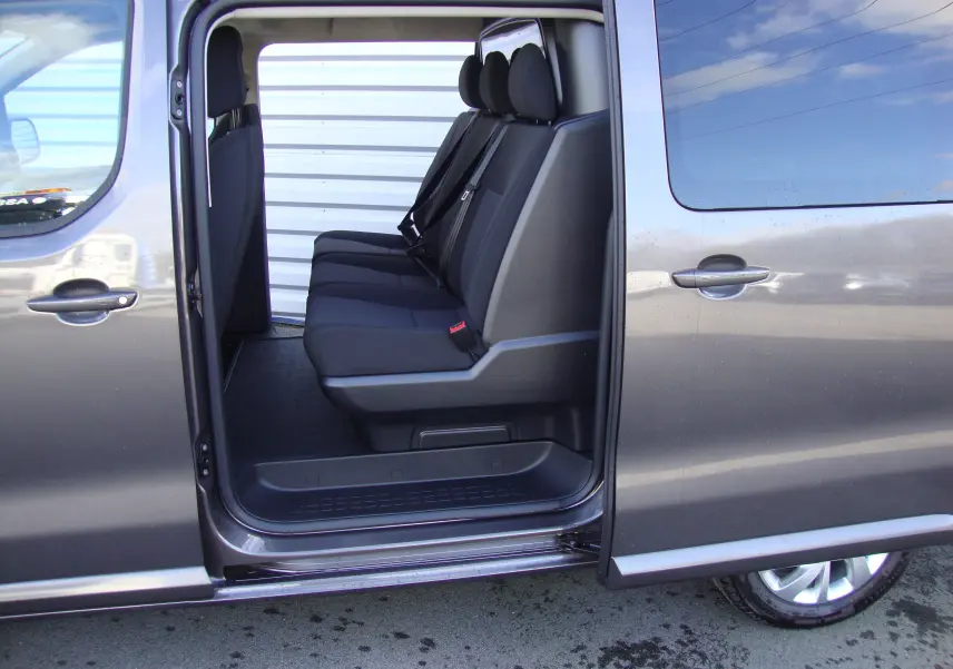 Vue latérale gauche sur l'ouverture de la porte coulissante d'un Citroën Jumpy XL gris platinum, montrant les sièges arrière noirs.