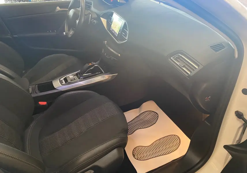 Intérieur avant droit d'une Peugeot 308 blanche 2020, sièges noirs, console centrale avec écran tactile et levier de boîte automatique.