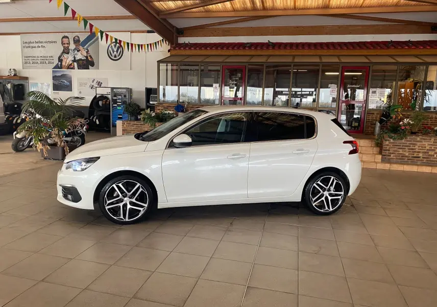 Peugeot 308 blanche vue de profil côté gauche, en intérieur, avec jantes alliage et vitres teintées.