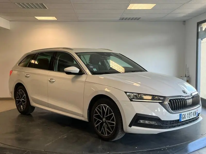 Vue 3/4 avant droite d'une Skoda Octavia Combi blanche Cristal spéciale en intérieur, avec jantes alu et calandre chromée.