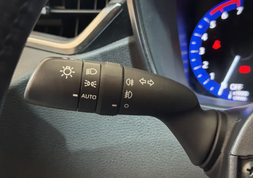 Gros plan sur la commande des phares avec réglages automatiques, dans l'habitacle gris d'une Toyota Corolla hybride 2021.