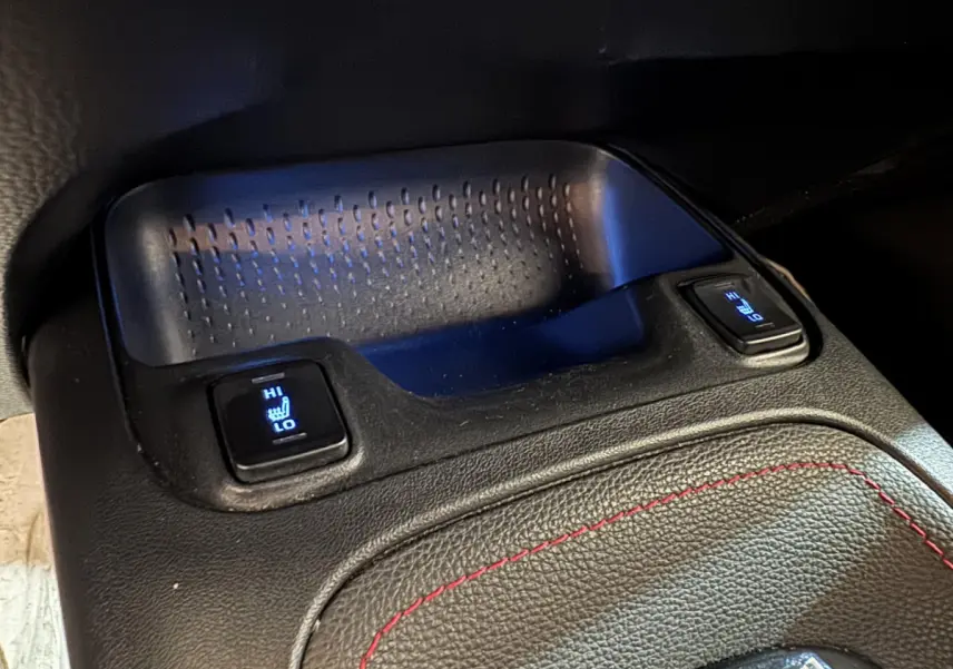 Gros plan sur les commandes de sièges chauffants arrière avec éclairage bleu sur la console centrale en cuir noir.