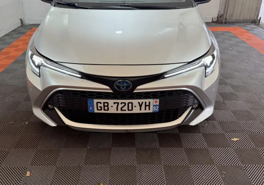 Vue frontale d'une Toyota Corolla Hybride 122h Collection gris clair avec calandre noire et phares LED fins.