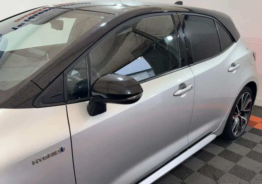 Vue de profil côté gauche d'une Toyota Corolla Hybride gris clair avec toit noir et rétroviseur noir brillant.