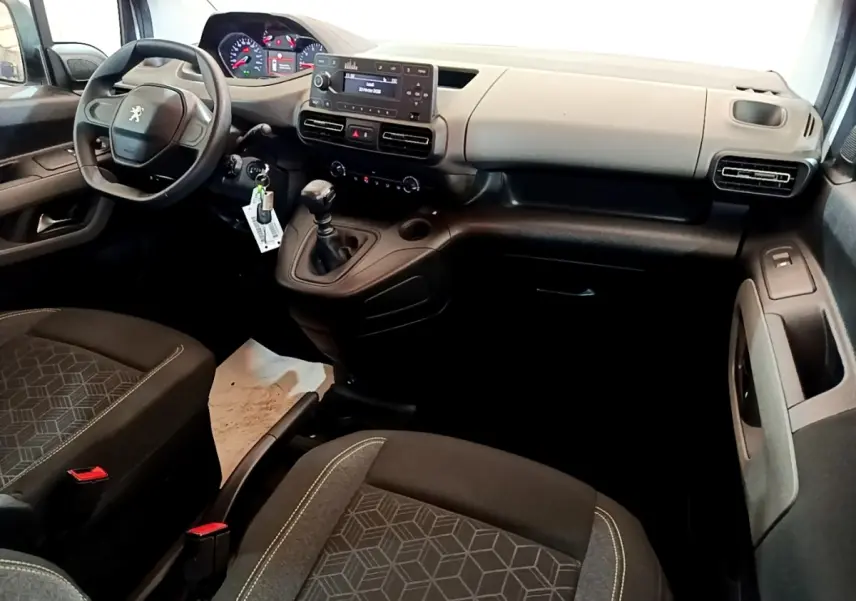 Vue intérieure avant droite du Peugeot Rifter 2019, tableau de bord gris clair et sièges noirs avec motifs géométriques.