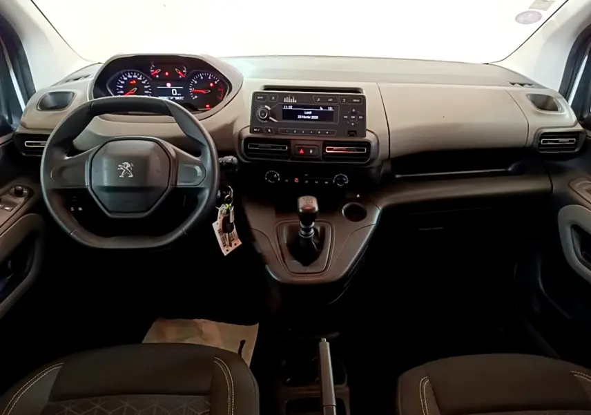 Vue intérieure avant du Peugeot Rifter blanc 2019, tableau de bord noir avec volant, levier de vitesse manuel et écran central.