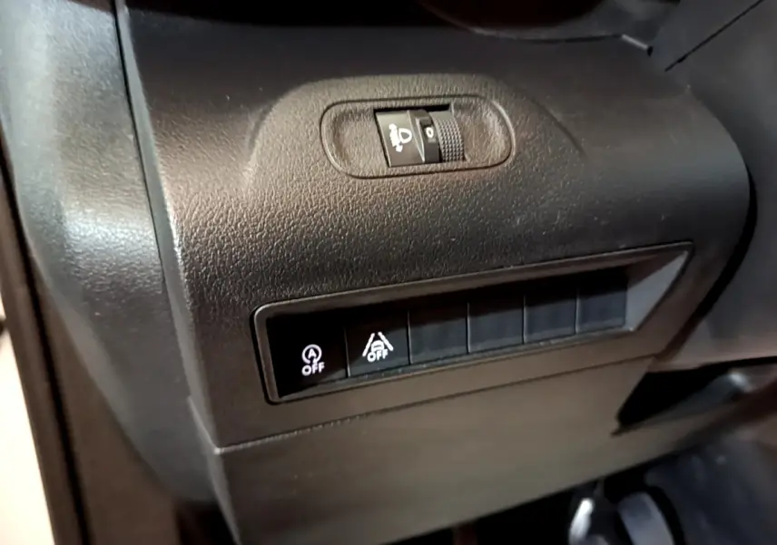 Gros plan sur les commandes de réglage des phares et désactivation de l'assistance au freinage du Peugeot Rifter blanc 2019.