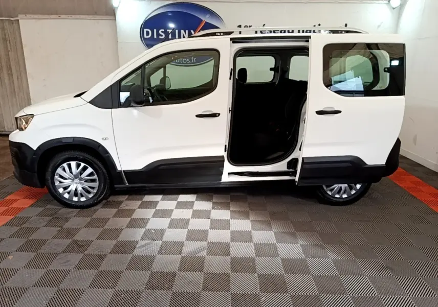 Vue latérale droite d'un Peugeot Rifter blanc 2019 avec porte coulissante arrière ouverte en intérieur showroom.