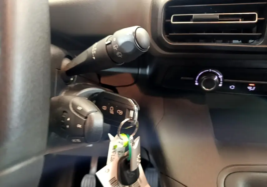 Gros plan intérieur sur la colonne de direction et clé de contact du Peugeot Rifter blanc, avec commande d’essuie-glace et ventilation.