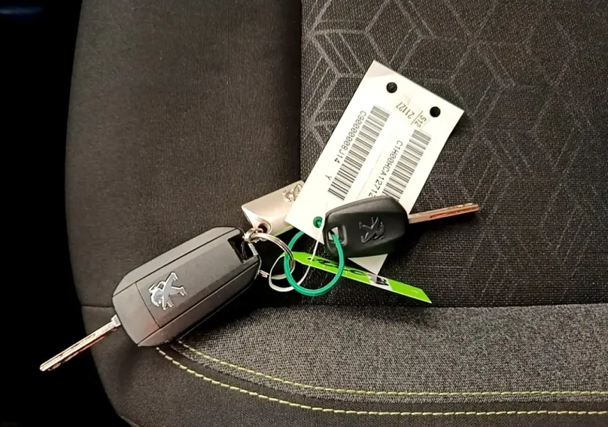 Jeu de clés Peugeot posé sur un siège tissu noir avec surpiqûres jaunes, sans vue directe du véhicule.